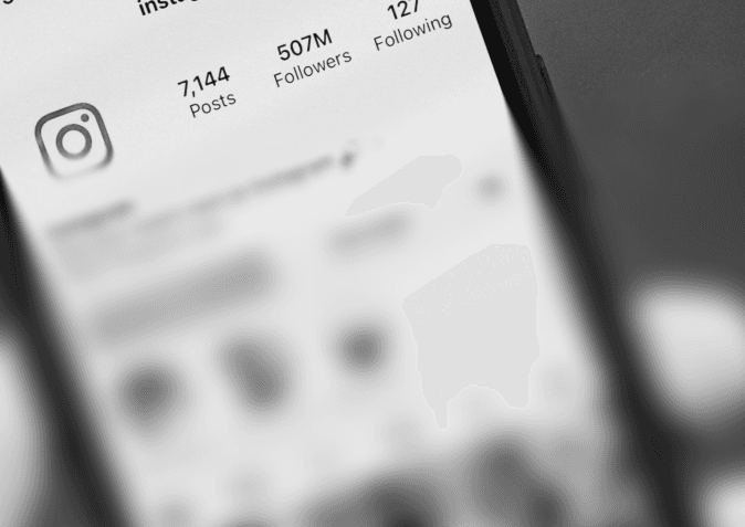 A blurred phone screen showing an Instagram profile with post, follower, and following counts