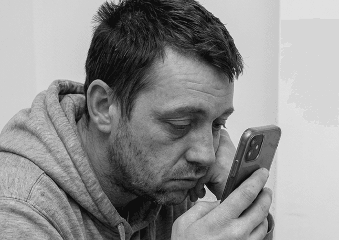 A man looking down at his phone with a hesitant expression