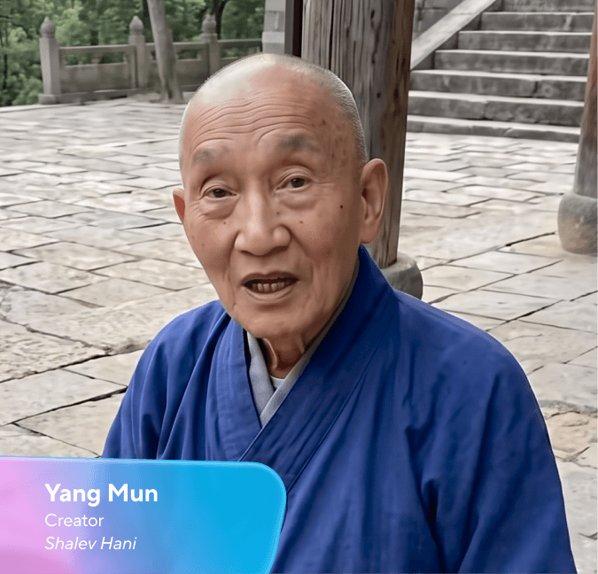 Yang Mun, an elderly bald person wearing a blue robe, speaking on a stone patio.