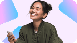 A smiling young woman in a green bomber jacket holds a white smartphone.