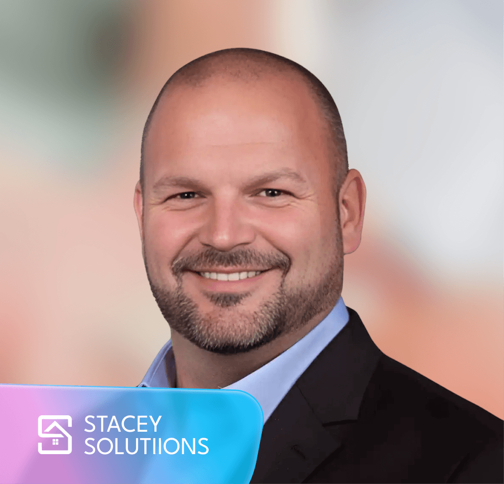 Smiling bald man with a beard in a suit, with the "STACEY SOLUTIIONS" logo.