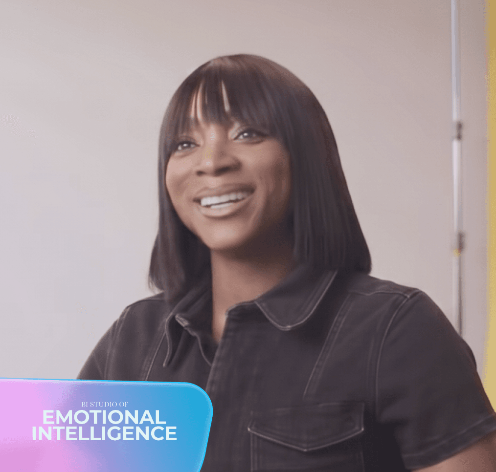 Isang nakangiting babaeng Black na may maitim na buhok at bangs ang nakasuot ng madilim na kamiseta; nasa ibabang kaliwa ang graphic na "BI STUDIO OF EMOTIONAL INTELLIGENCE".